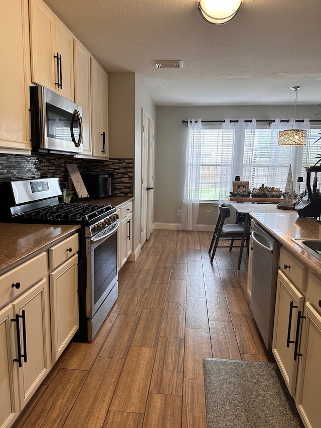 kitchen with pendant lighting, light wood-type flooring, a textured ceiling, appliances with stainless steel finishes, and tasteful backsplash