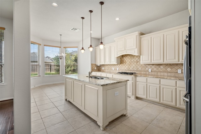 kitchen with light stone countertops, sink, a chandelier, hanging light fixtures, and an island with sink