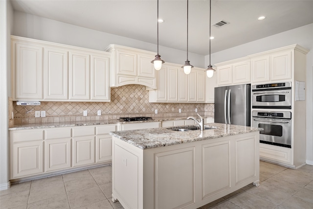 kitchen with a center island with sink, sink, light stone countertops, appliances with stainless steel finishes, and tasteful backsplash