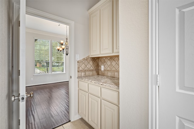 bar featuring light stone countertops, light hardwood / wood-style flooring, a notable chandelier, crown molding, and decorative backsplash