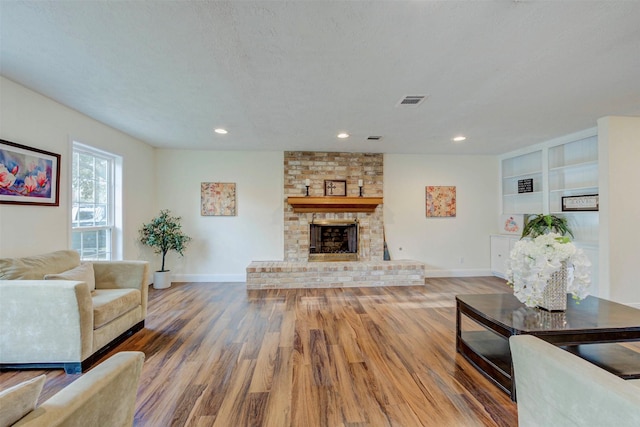 living room featuring a fireplace, built in shelves, a textured ceiling, and hardwood / wood-style flooring