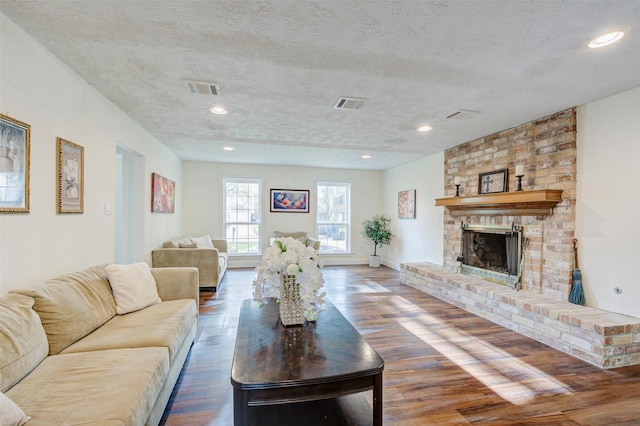 living room with dark hardwood / wood-style floors, a textured ceiling, and a brick fireplace