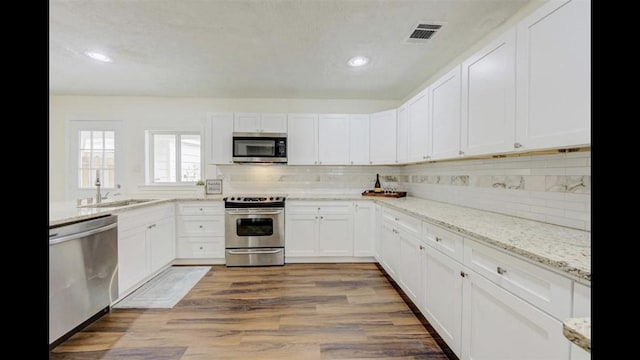 kitchen featuring wood-type flooring, sink, appliances with stainless steel finishes, light stone counters, and white cabinetry