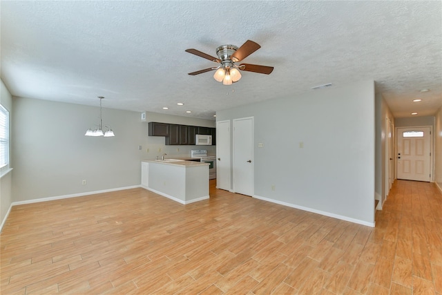 unfurnished living room featuring ceiling fan with notable chandelier, light wood-type flooring, and a textured ceiling