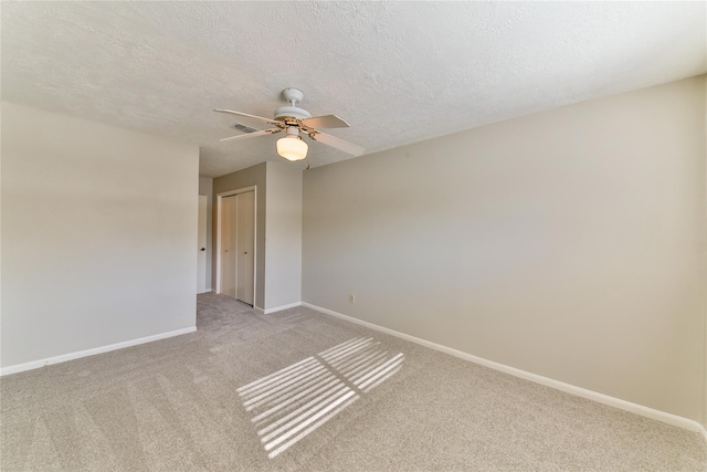 spare room featuring ceiling fan, light colored carpet, and a textured ceiling