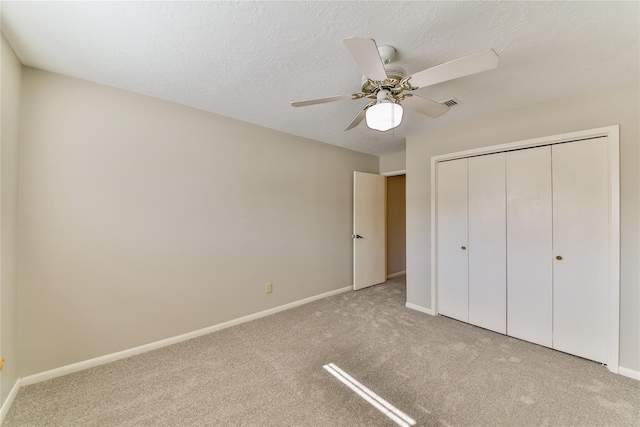 unfurnished bedroom featuring ceiling fan, a closet, light colored carpet, and a textured ceiling