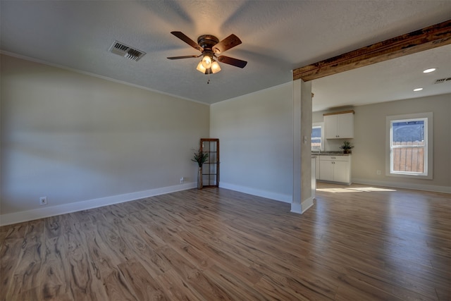 spare room with ceiling fan, light hardwood / wood-style floors, beam ceiling, and a textured ceiling