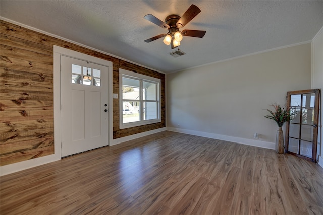 foyer entrance with hardwood / wood-style floors, crown molding, wooden walls, ceiling fan, and a textured ceiling