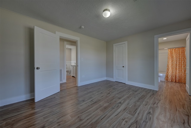 unfurnished bedroom with a closet, a textured ceiling, connected bathroom, and light hardwood / wood-style flooring