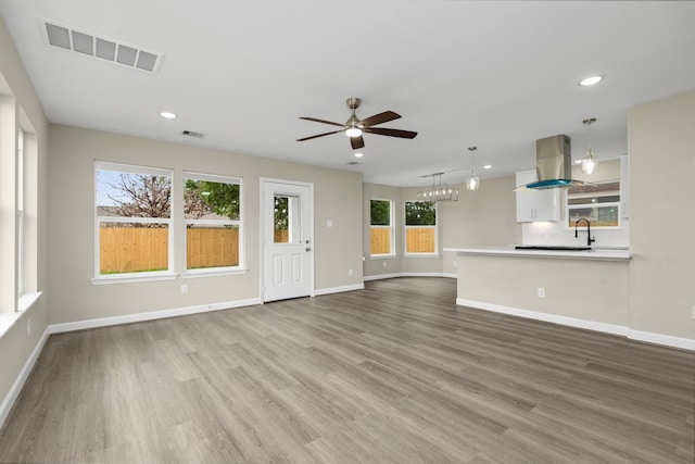 unfurnished living room with ceiling fan with notable chandelier and light hardwood / wood-style floors