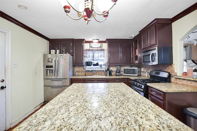 kitchen featuring sink, decorative backsplash, appliances with stainless steel finishes, light stone counters, and a chandelier