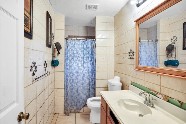 bathroom with tile patterned floors, vanity, a textured ceiling, tile walls, and toilet