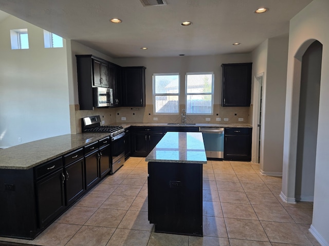 kitchen with light stone countertops, a center island, tasteful backsplash, light tile patterned flooring, and appliances with stainless steel finishes