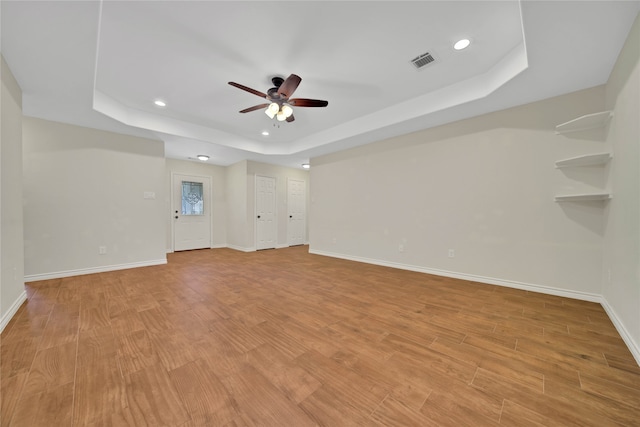 empty room with a raised ceiling, ceiling fan, and light hardwood / wood-style flooring