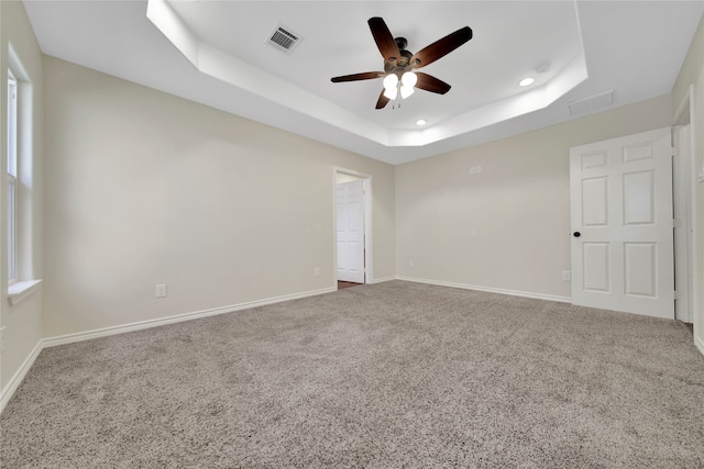 carpeted empty room featuring ceiling fan and a raised ceiling