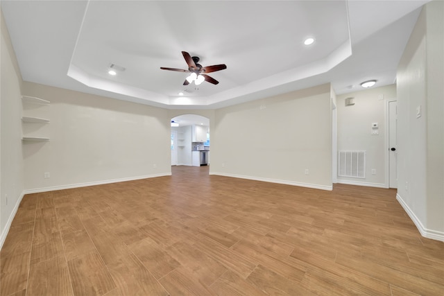 unfurnished living room with a tray ceiling, ceiling fan, and light wood-type flooring