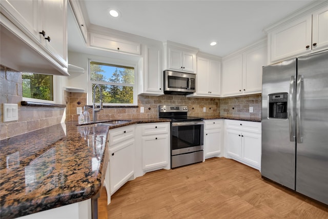 kitchen featuring decorative backsplash, appliances with stainless steel finishes, dark stone counters, light hardwood / wood-style floors, and white cabinetry