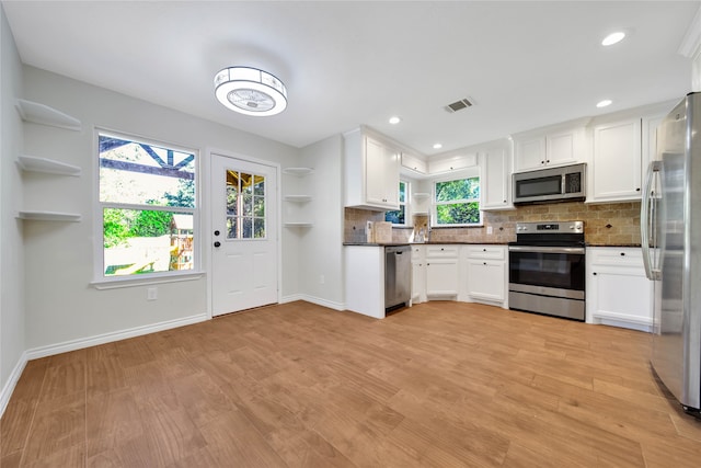 kitchen with tasteful backsplash, white cabinets, stainless steel appliances, and light hardwood / wood-style floors