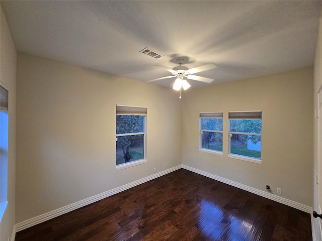 empty room featuring plenty of natural light, ceiling fan, and dark wood-type flooring