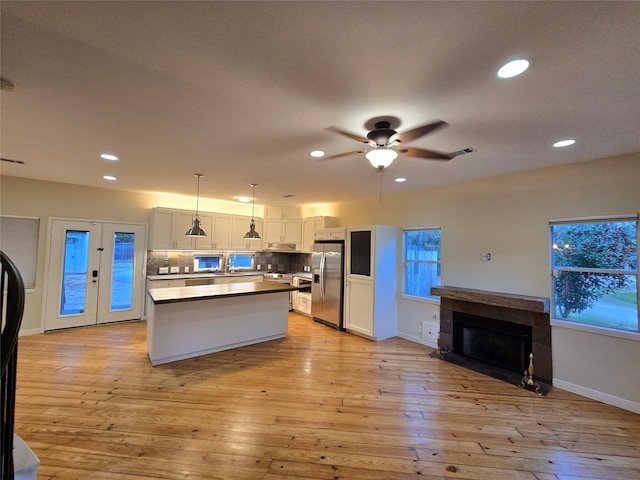 kitchen featuring backsplash, white cabinets, light hardwood / wood-style flooring, decorative light fixtures, and stainless steel appliances