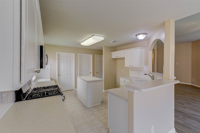 kitchen featuring kitchen peninsula, light hardwood / wood-style flooring, a center island, white cabinetry, and range with gas stovetop