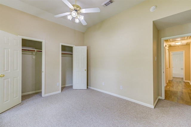 unfurnished bedroom featuring light colored carpet, vaulted ceiling, ceiling fan, and multiple closets