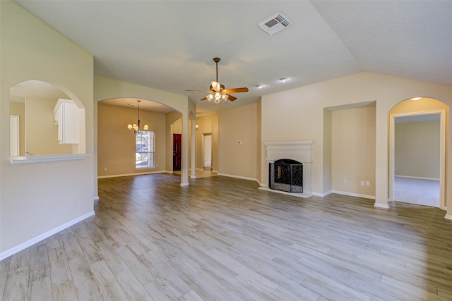 unfurnished living room featuring ceiling fan with notable chandelier, light hardwood / wood-style floors, and vaulted ceiling