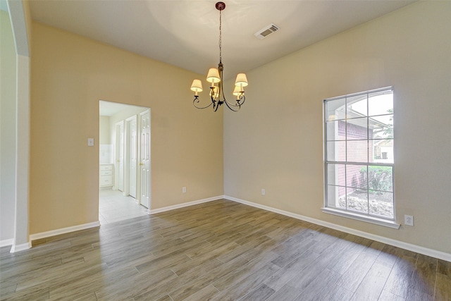 spare room with wood-type flooring and an inviting chandelier