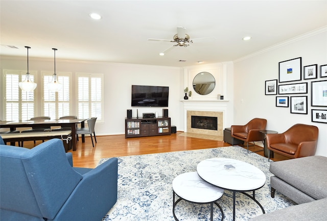 living room featuring a fireplace, wood-type flooring, ceiling fan, and ornamental molding