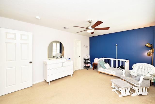 carpeted bedroom with ceiling fan and a nursery area