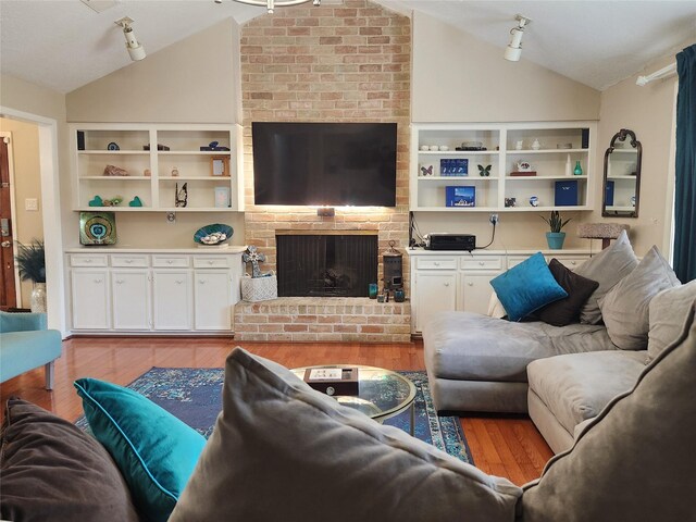 living room with a brick fireplace, track lighting, vaulted ceiling, and light hardwood / wood-style flooring