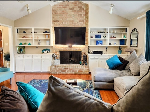 living room featuring track lighting, a fireplace, light hardwood / wood-style flooring, and vaulted ceiling