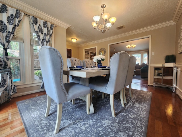 dining room with visible vents, hardwood / wood-style flooring, a textured ceiling, an inviting chandelier, and crown molding