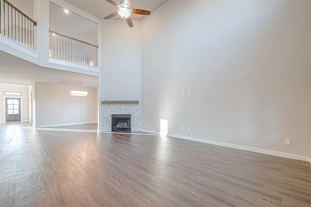 unfurnished living room with a tile fireplace, a high ceiling, hardwood / wood-style flooring, and ceiling fan