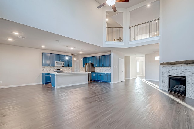 unfurnished living room featuring ceiling fan, a fireplace, a towering ceiling, and hardwood / wood-style flooring