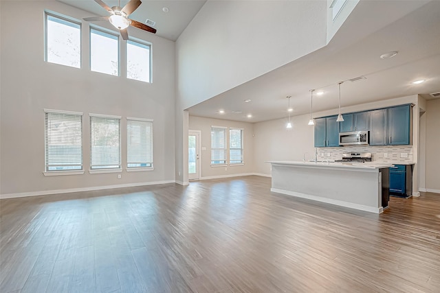 unfurnished living room with ceiling fan, a high ceiling, and hardwood / wood-style flooring