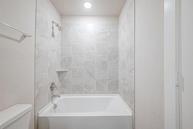 bathroom with tiled shower / bath combo, toilet, and a textured ceiling