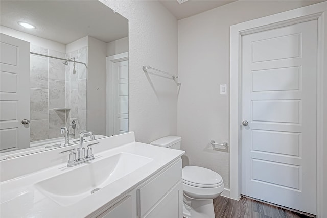 bathroom featuring toilet, vanity, wood-type flooring, and tiled shower