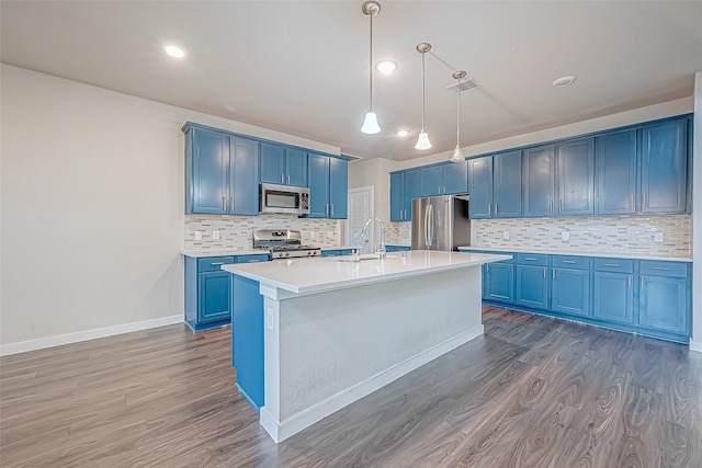 kitchen with blue cabinetry, stainless steel appliances, dark hardwood / wood-style floors, and an island with sink