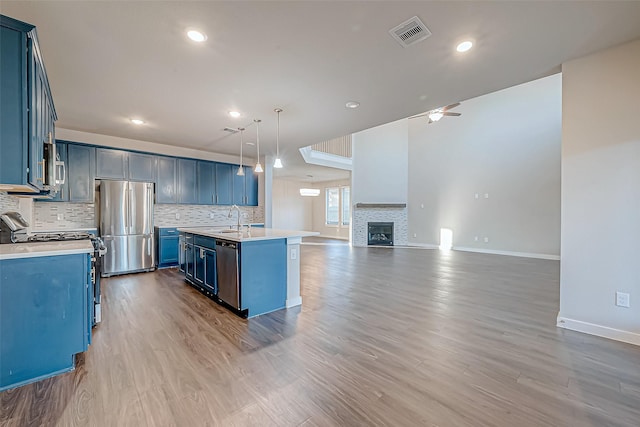 kitchen with blue cabinetry, light hardwood / wood-style flooring, pendant lighting, and appliances with stainless steel finishes