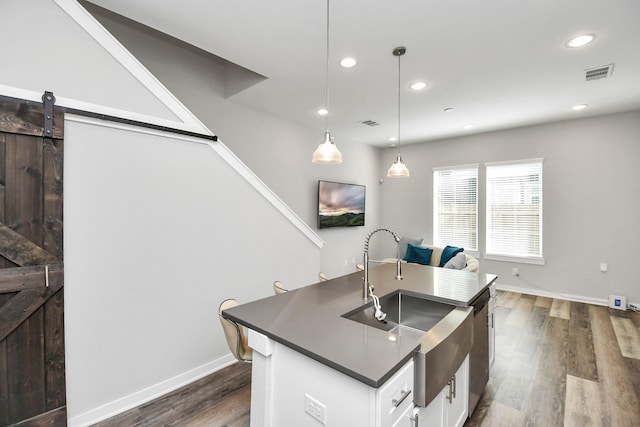 kitchen featuring dark wood-type flooring, a barn door, decorative light fixtures, white cabinetry, and an island with sink