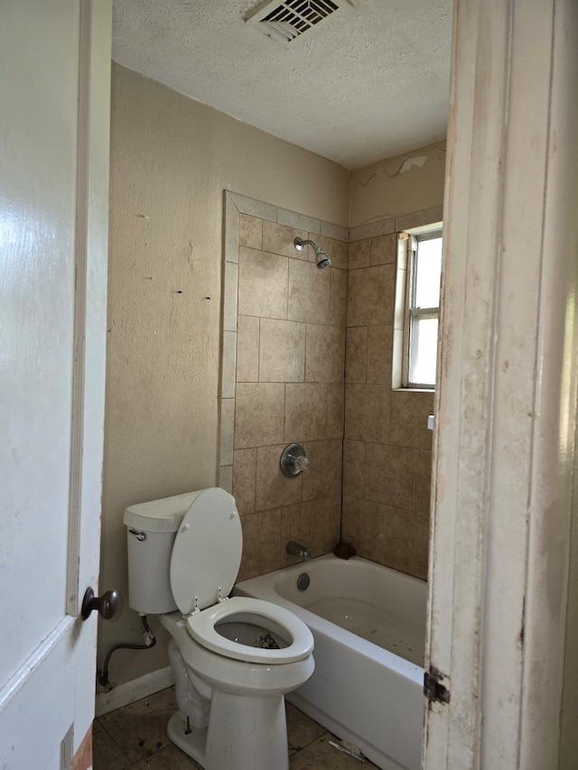 bathroom with tile patterned floors, a textured ceiling, tiled shower / bath combo, and toilet