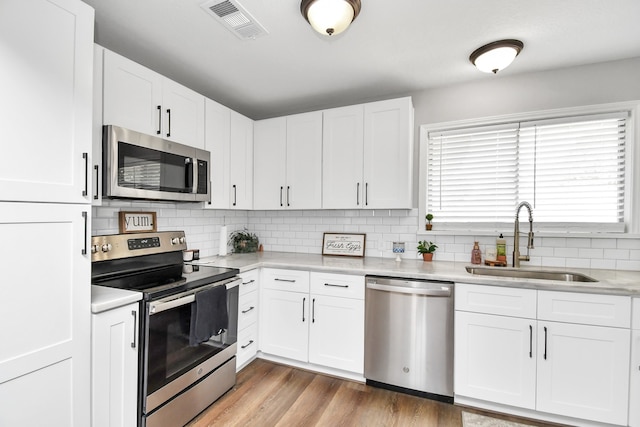 kitchen with white cabinets, stainless steel appliances, light hardwood / wood-style floors, and sink