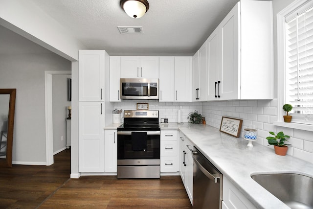 kitchen with white cabinetry, tasteful backsplash, dark hardwood / wood-style floors, a textured ceiling, and appliances with stainless steel finishes