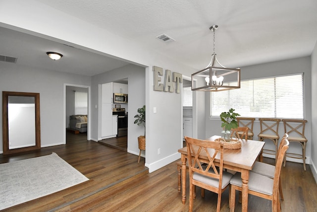 dining space with a textured ceiling, a notable chandelier, and dark wood-type flooring