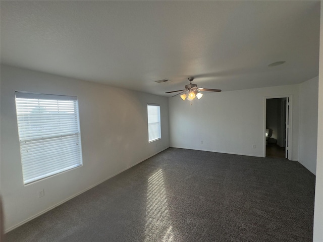 spare room featuring dark colored carpet, a wealth of natural light, and ceiling fan