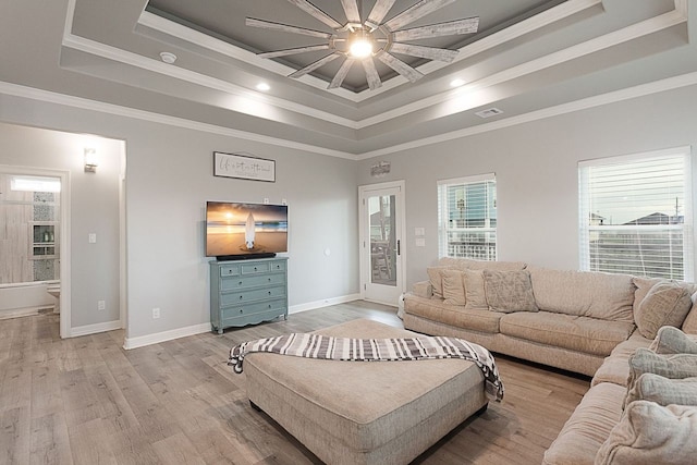 living room with ceiling fan, a raised ceiling, light wood-type flooring, and crown molding