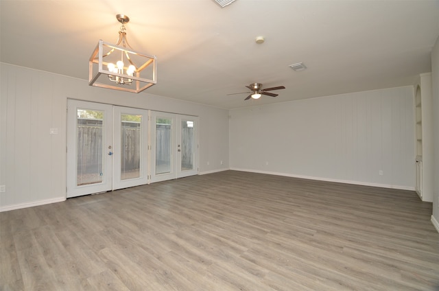 unfurnished room featuring hardwood / wood-style flooring, ceiling fan with notable chandelier, wood walls, and french doors