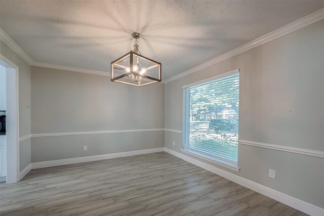 empty room featuring a chandelier, a textured ceiling, light wood-type flooring, and ornamental molding