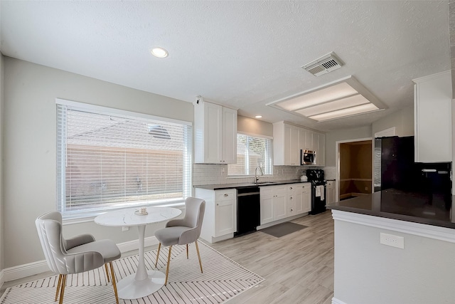 kitchen featuring backsplash, light hardwood / wood-style flooring, white cabinetry, and black appliances